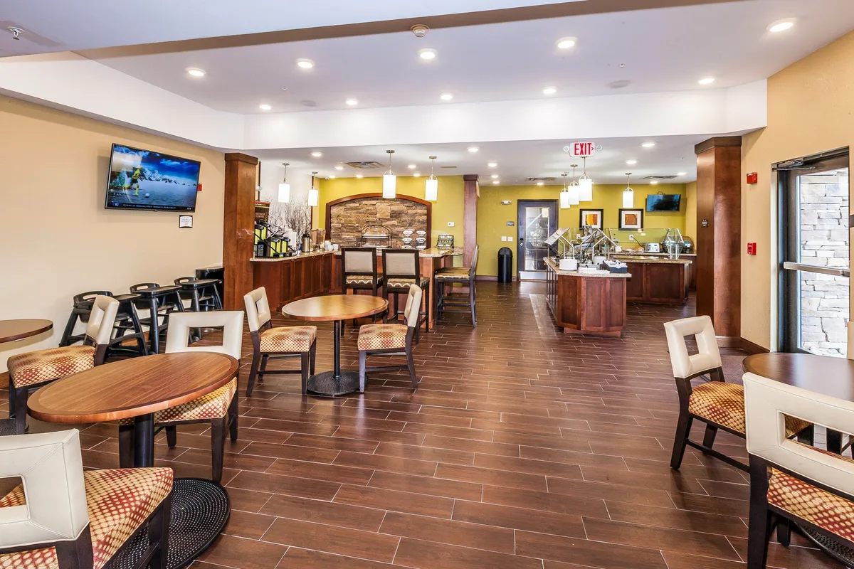 A spacious, comfortable lounge with a central seating area, a visible reception counter, a TV display, and a decorative stone wall. Guests relax and socialize, some with laptops, indicating both leisure and productivity.