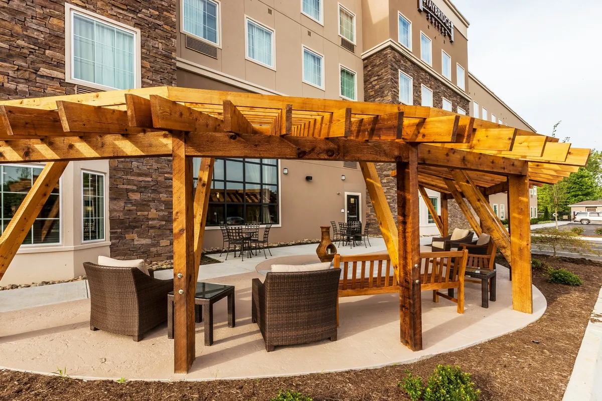 An inviting exterior seating area under a wooden pergola, complete with comfortable chairs and a decorative vase. The space is ideal for relaxing, socializing, or enjoying a drink outdoors, and the warm ambiance suggests it’s perfect for evening mingling or morning coffee with fellow guests.