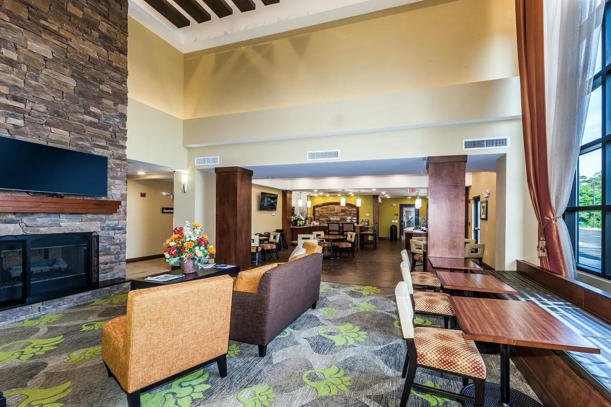 A cozy dining and lounge space with a prominent stone fireplace, elegant floral decorations, and wooden tables arranged for group or family seating, ideal for socializing and casual dining.