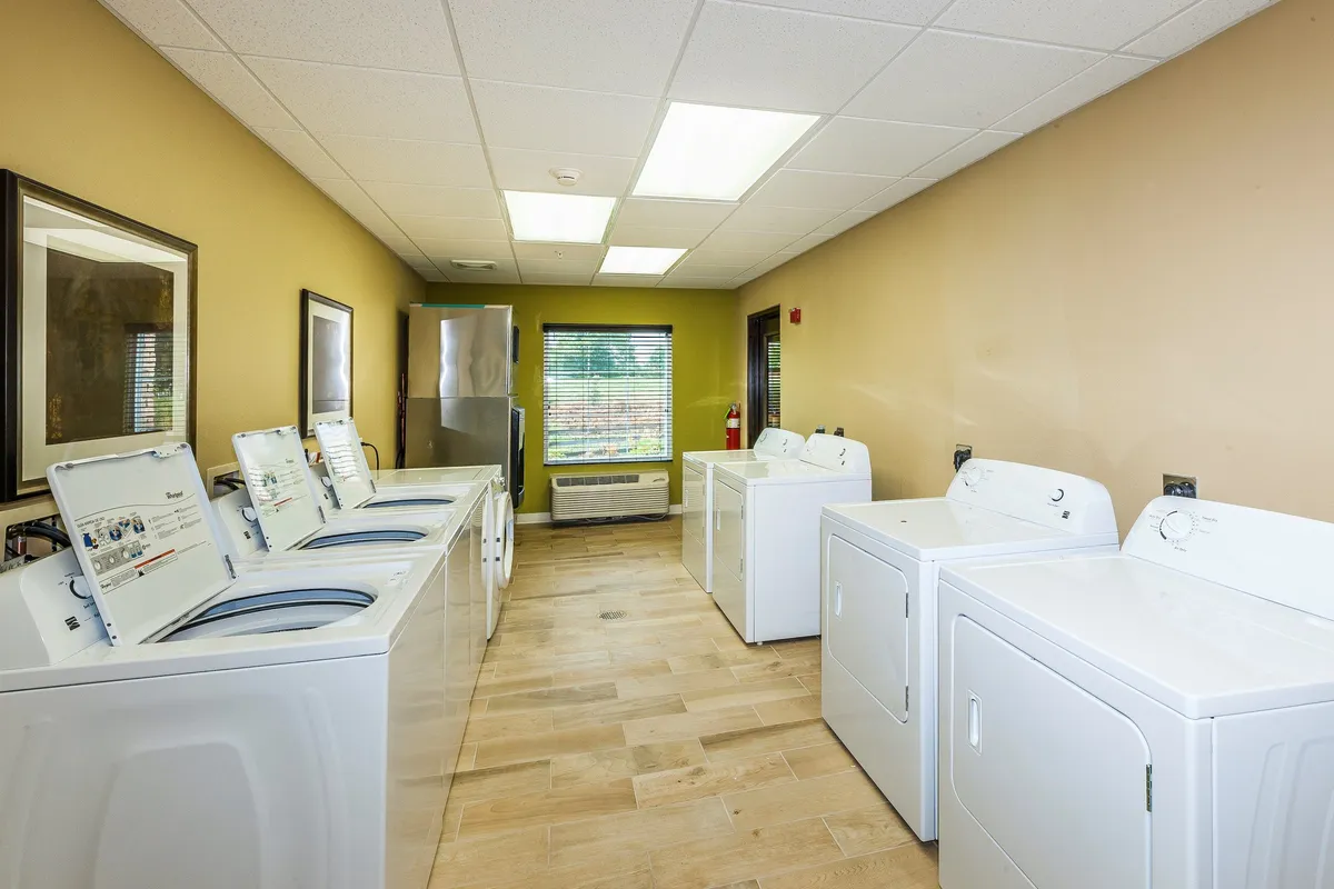 This image depicts a practical laundry area inside the property, featuring washing machines, dryers, a window with a view, and an air conditioning unit. The mood is efficient and comfortable, tailored for guests who may have extended stays or prioritize amenities that enhance convenience.